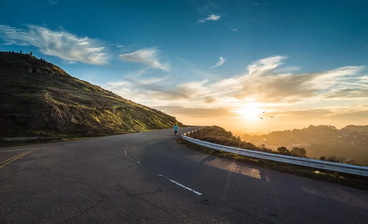 Läufer auf einer Bergstraße bei Sonnenaufgang – Sinnbild für den Weg zum Ziel